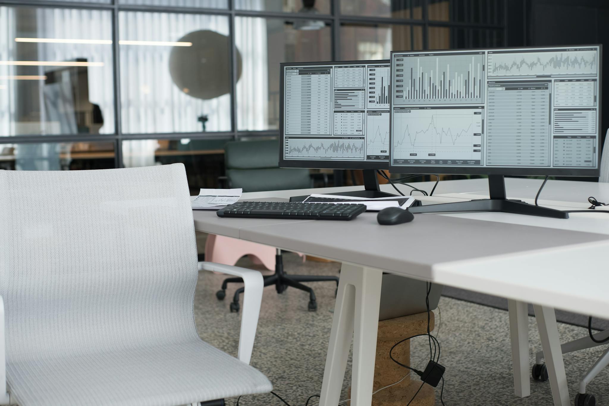 A modern office desk with dual monitors displaying data and an ergonomic chair, perfect for a productive workspace.